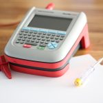Image shows a PAT testing machine with probe, sitting on a worktop with some paperwork nearby.